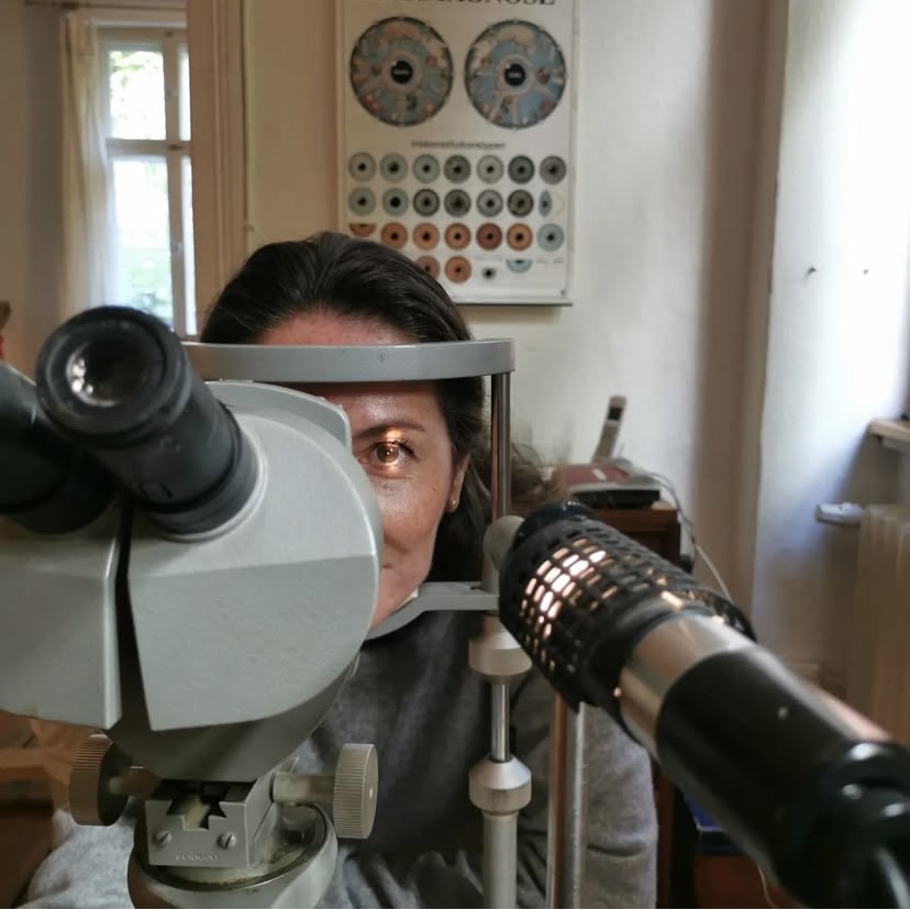 Eine Person sitzt an einem Mikroskop und ihr wird ins Auge geschaut