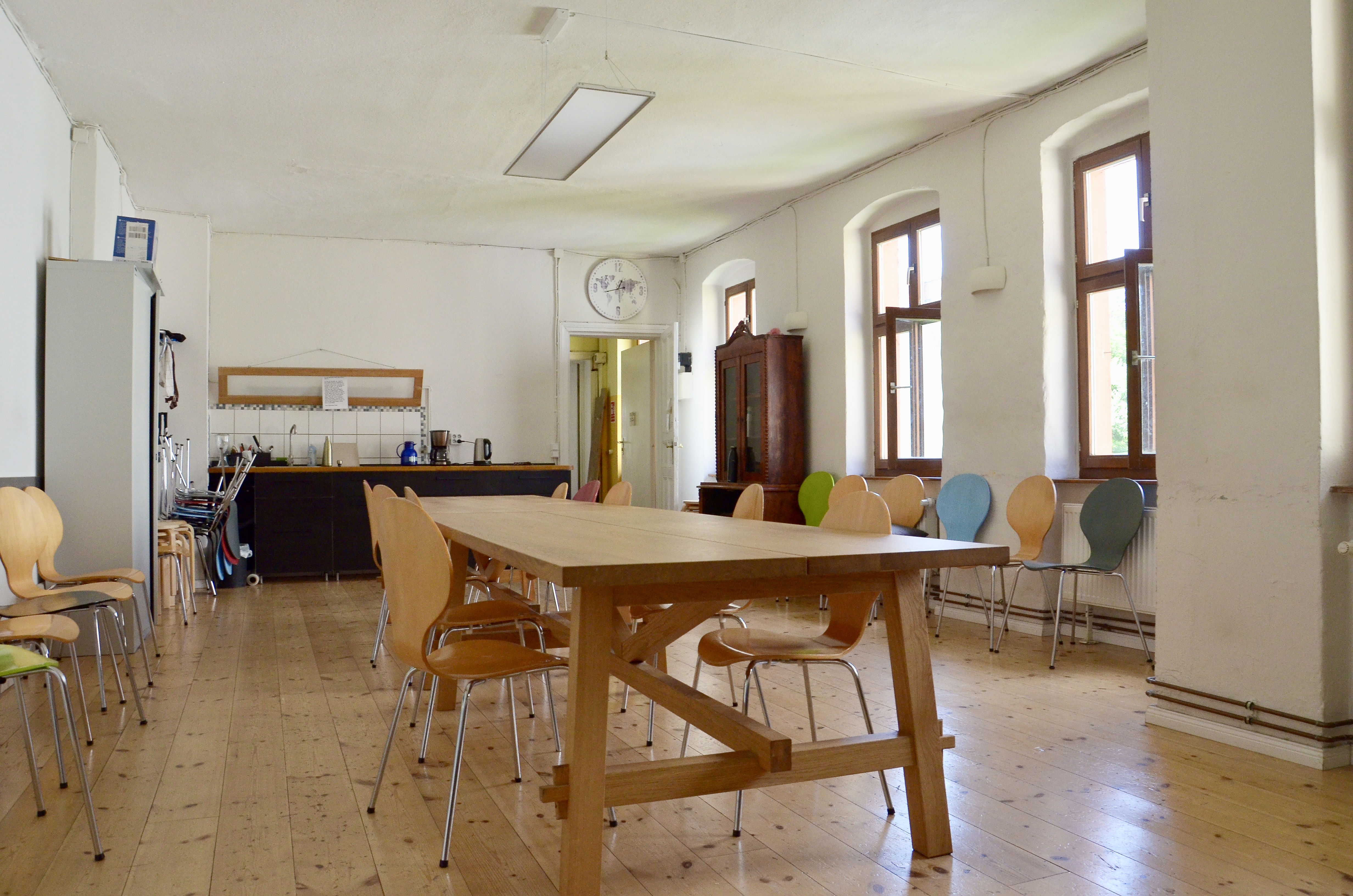 Ein heller und großer Raum mit einem großem Tisch mittig im Raum und Stühlen herum