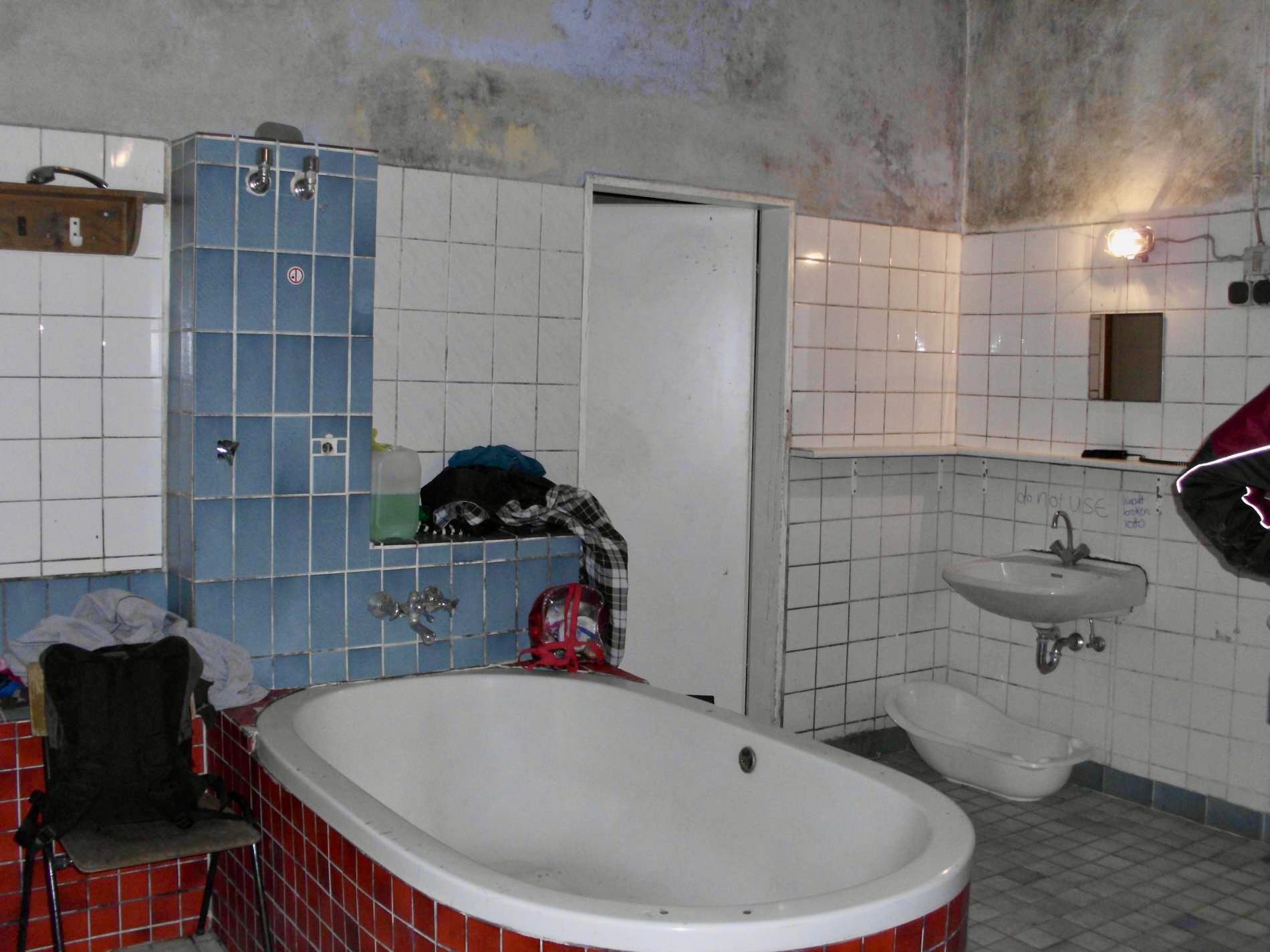 Großer Raum mit einer großen Badewanne in der Mitte, weißen Fliesen und blauen Wandfliesen.